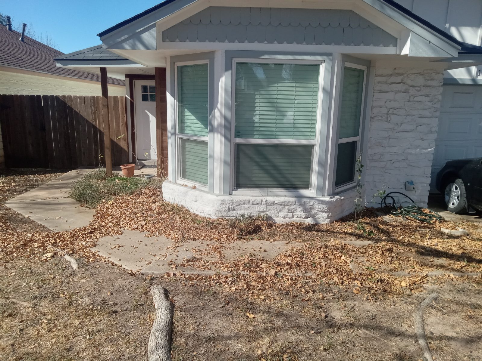 Front flower bed covered in dead leaves before cleanup