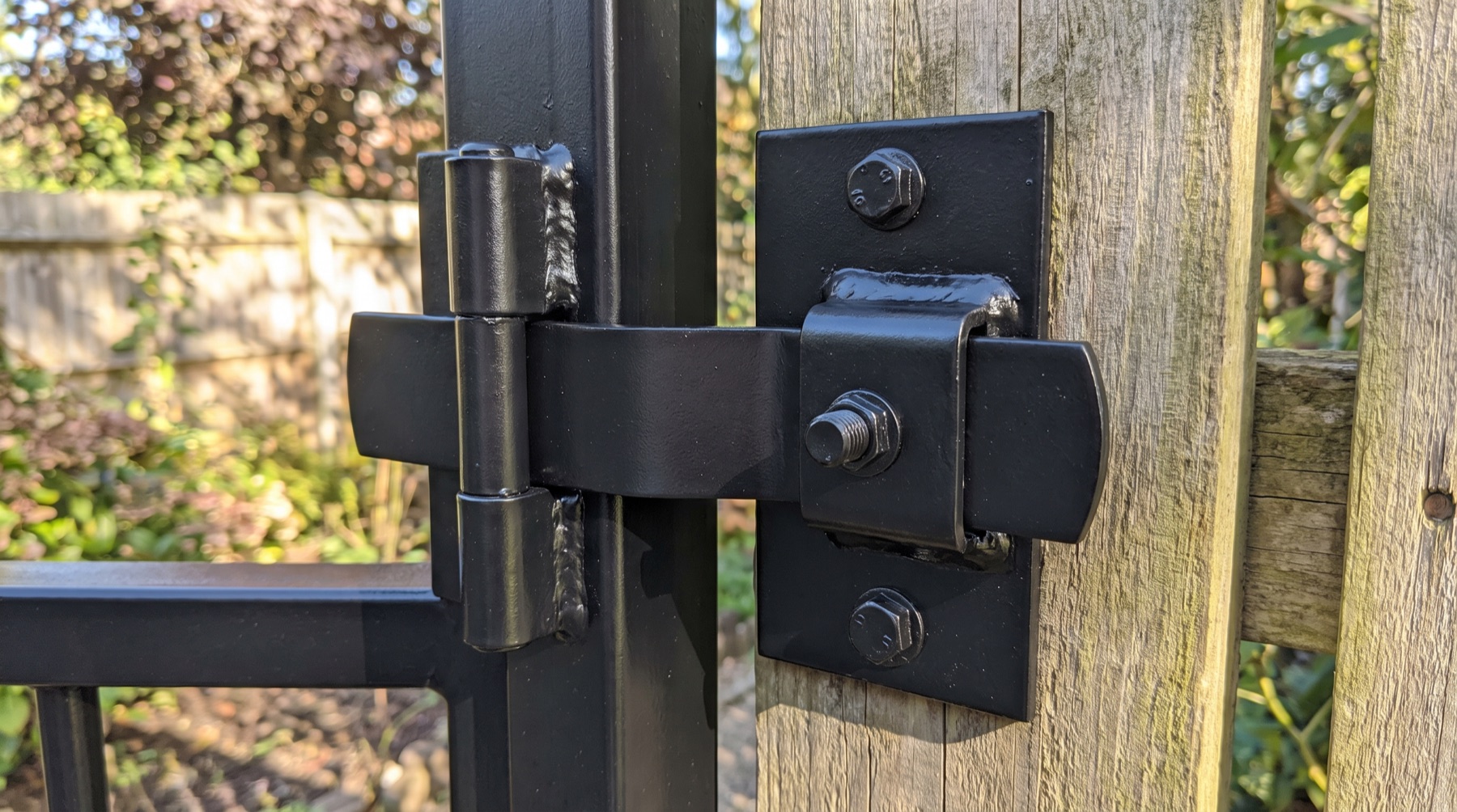 Repaired black steel gate hinge and latch on a fence post